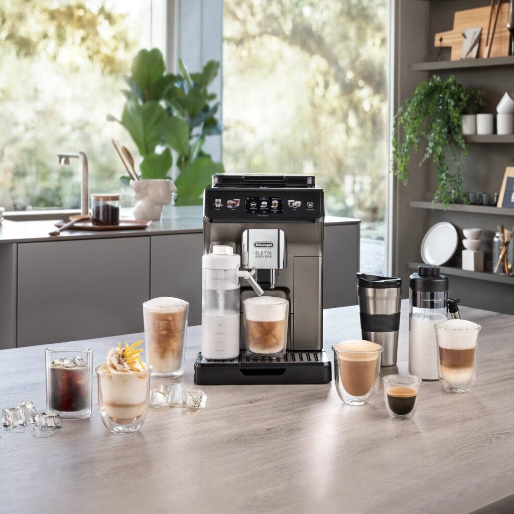 De'Longhi Eletta Explore ECAM450.86.T Kaffeevollautomat in Titanium, Ansicht in der Küche mit Reisebecher, Milchkaraffen und Getränken